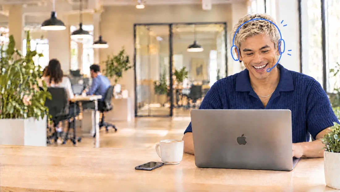 Lachende Credifin-medewerker met headset helpt een klant aan de telefoon terwijl hij het incassodossier op zijn MacBook verwerkt